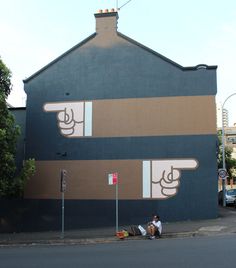 a man sitting on the sidewalk in front of a building with two fingers painted on it