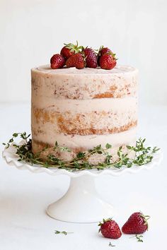 a cake with strawberries on top is sitting on a white plate and has greenery around it