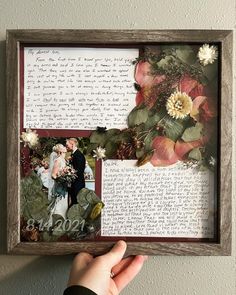 a person holding up a framed photo with flowers and leaves in the frame on top of it