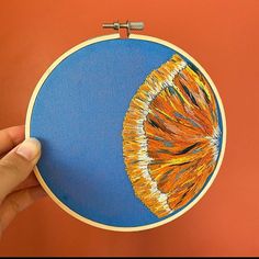 a hand holding up a small embroidery piece with an orange and blue design on it