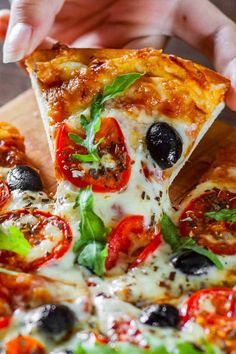 a person holding a slice of pizza with olives, peppers and basil on it