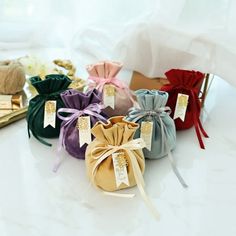 several small pouches with ribbons tied around them on a white counter top next to some gold and silver items