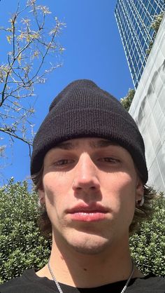 a young man wearing a black beanie looking at the camera with a blue sky in the background