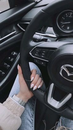 a woman sitting in the driver's seat of a car with her hands on the steering wheel