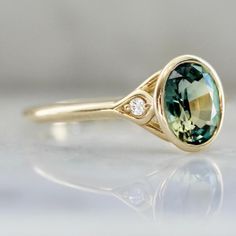 Why I Love It: This divine morsel features an ethereal 1.43 carat oval cut parti sapphire center with stunning hues of green, blue, and yellow. A perfectly matched pair of white round brilliant cut diamonds in the shoulders and delicious 14k Yellow Gold finish off this stunning engagement ring. Sits low and flush to the finger. The Details: 14k Yellow Gold 1.43 Carat Green Oval Cut Parti Sapphire Madagascar Origin .04 Carats Total of White Round Brilliant Cut Canadian Diamonds Current Ring Size Fine Jewelry Green Sapphire Ring With Rose Cut Diamonds, Green Sapphire Ring With Rose Cut Diamonds, Heirloom Green Sapphire Ring With Diamonds, Parti Sapphire, Green Oval, Stunning Engagement Ring, Round Brilliant Cut Diamond, Rose Cut, Oval Cut