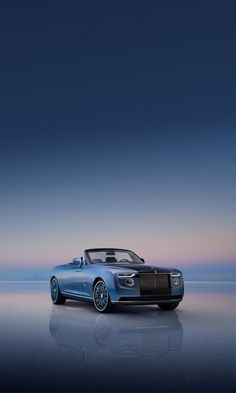 a blue rolls royce parked in front of the ocean at dusk with its roof down