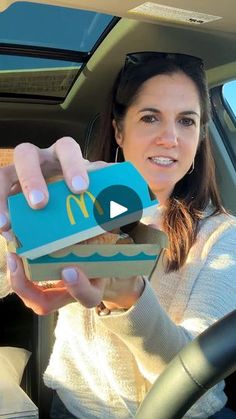 a woman holding up a box with a mcdonald's sign on it in the back seat of a car