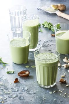 three glasses filled with green smoothie sitting on top of a table next to nuts