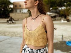 a woman standing on the beach with her eyes closed and wearing a yellow tank top