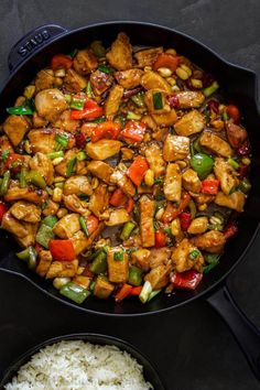 chicken and vegetable stir fry in a skillet next to rice on a black surface