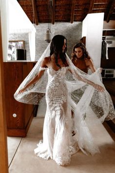 two women in wedding gowns are looking at each other with veils over their heads