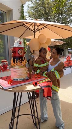 a woman and child standing next to a table with a fireman cake on it