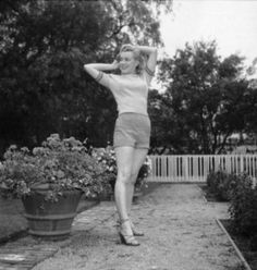 black and white photograph of a woman in short shorts posing for the camera with her arms behind her head