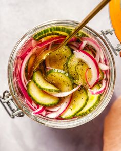 a person holding a spoon in a jar filled with pickles and cucumbers