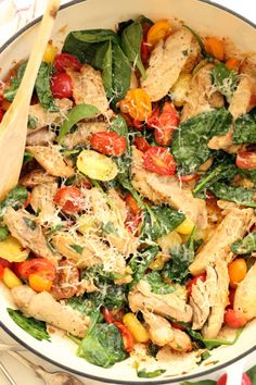 a salad with chicken, tomatoes, spinach and parmesan cheese in a white bowl