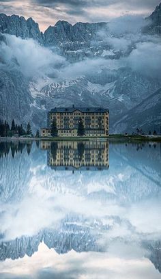 a large building sitting on top of a lake surrounded by mountains