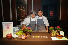 two men standing next to each other in front of a table with flowers and plants on it