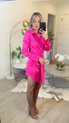 a woman taking a selfie in her living room wearing a pink dress and high heels