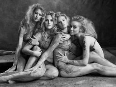 four women sitting on the ground covered in mud, with their arms around each other