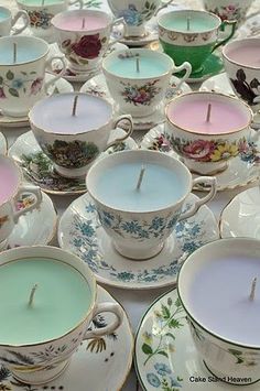 teacups with candles in them are sitting on a table top, surrounded by other cups and saucers