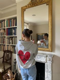 a woman standing in front of a mirror with a heart on it's hoodie