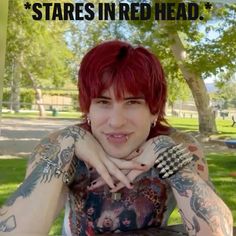 a woman with red hair and tattoos sitting in a park