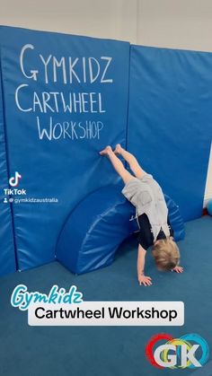 a young boy is climbing on a blue trampoline at the gym and has his hands in the air