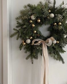 a christmas wreath hanging on the wall next to a door with ribbon and ornaments around it