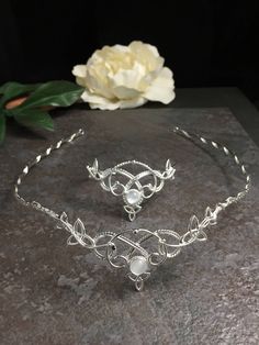 two pieces of silver jewelry sitting on top of a stone slab next to a flower