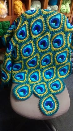 there is a blue and yellow peacock blanket on the back of a chair with yarns in the background