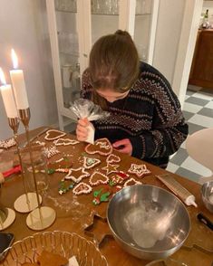 a woman decorating gingerbreads on a table with candles and other holiday decorations