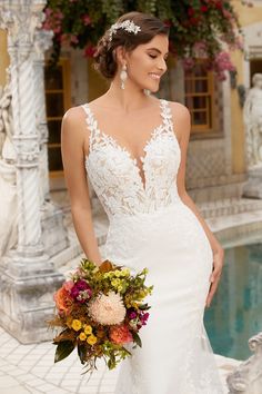 a woman in a wedding dress standing next to a fountain with flowers on her bouquet