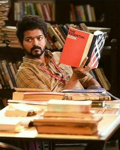 a man sitting at a table with a book in front of him and holding it up to his face