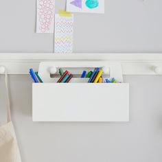 a white wall mounted shelf with books and pencils in the bottom drawer, next to a pair of scissors