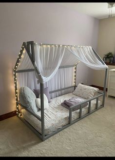 a canopy bed with white curtains and lights on the sides is in a room that has carpeted flooring