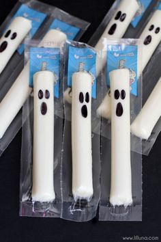 four white candles with black eyes and ghost faces in plastic wrappers on a table