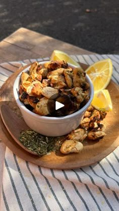 a bowl filled with food sitting on top of a wooden plate next to lemon wedges