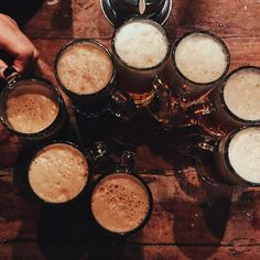 several mugs of beer are arranged on a wooden table, with one being filled