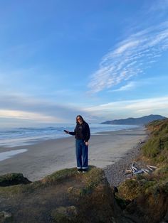 a man standing on top of a rock next to the ocean holding a cell phone