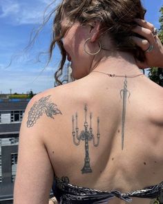 the back of a woman with tattoos on her upper and lower back, holding two candles