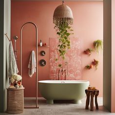 a bathroom with pink walls and an oval bathtub next to a plant hanging on the wall