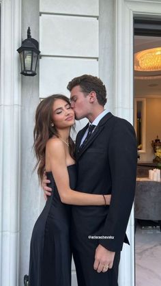 a man in a suit and tie kissing a woman wearing a black evening gown on the steps of a building