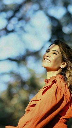 a woman in an orange shirt looking up into the sky with trees in the background