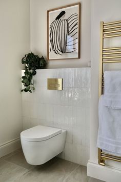 a white toilet sitting in a bathroom next to a towel rack and potted plant