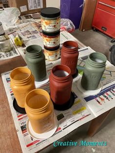 there are many different colored jars on the table with newspaper and other items around them