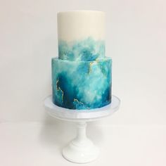 a three tiered cake with blue and white icing on a plate against a white background