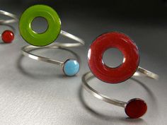 "Lifesaver in Orbit Ring: A lifesaver O-shape of bright cherry red enamel orbits a smaller burgundy red disc on a slender, sturdy and comfortable band of square sterling silver wire. This ring is A D J U S T A B L E to fit sizes 6-9 and can be stacked with other rings! Each ring is individually handcrafted and kiln-fired. The powdered glass enamel is kiln-fired onto copper discs 3/8\" (10 mm) in diameter and 3/16\" (5 mm) in diameter. The sturdy square style sterling wire band is hard soldered o Adjustable Red Enamel Rings, Orbit Ring, Blue Disc, Tangerine Orange, Fire Glass, Square Stud, Green Enamel, Support Handmade, Enamel Jewelry