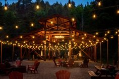 an outdoor dining area with lights strung from the ceiling and wooden benches on gravel ground