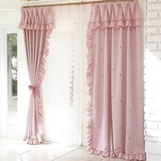 pink curtains with ruffles hanging from them in front of a white brick wall