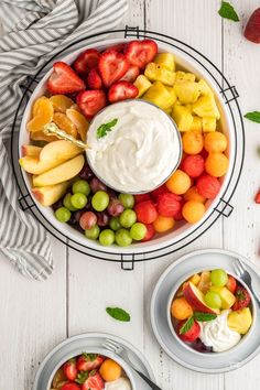 two bowls filled with fruit and dip on top of a white wooden table next to another bowl full of fruit